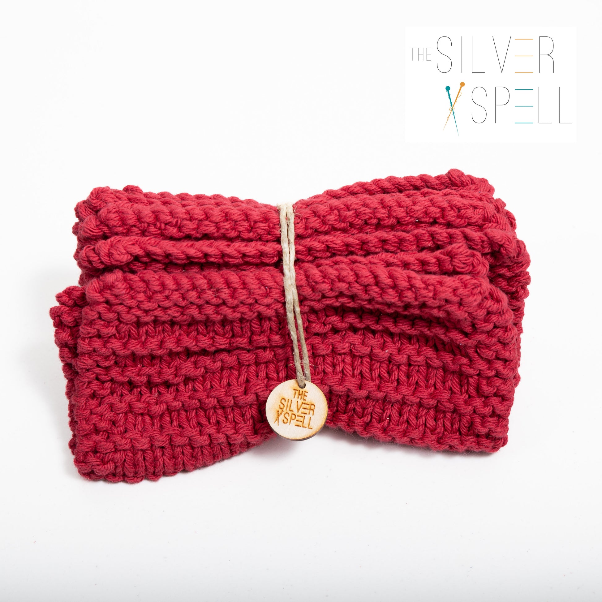 A red cotton washcloth with a bow in the middle, displayed on a white background, with a tag attached that reads 'The Silver Spell'.