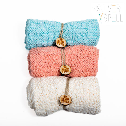 Three folded towels in blue, pink, and white, each with a decorative button on the front, placed side by side.