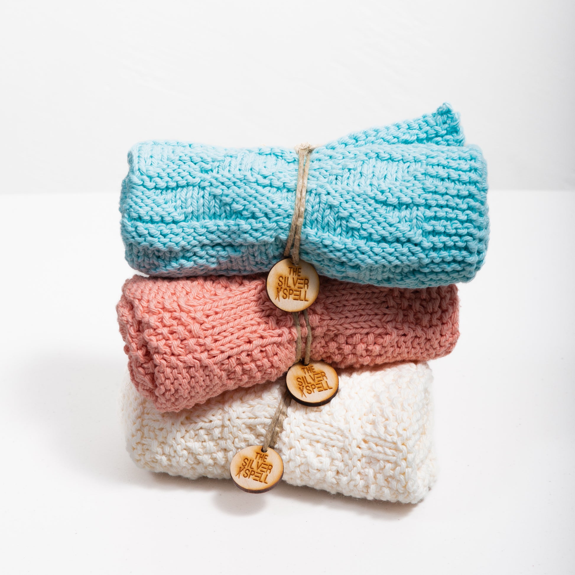 Three folded towels in blue, pink, and white, each with a decorative button on the front, placed side by side.