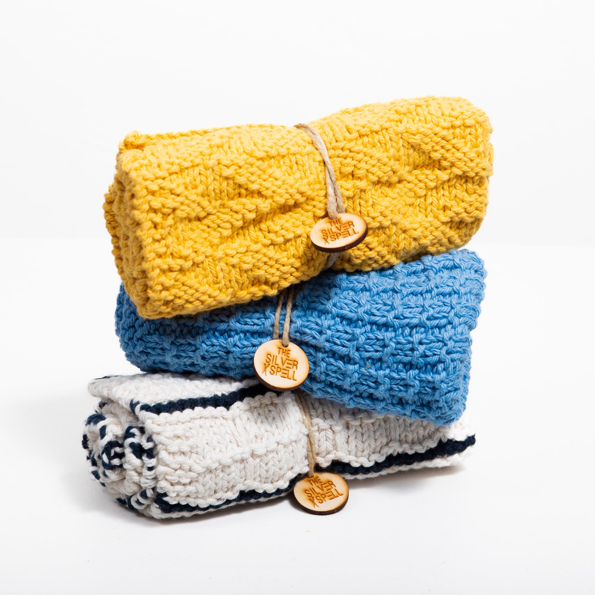 Three folded towels in yellow, blue, and white with black stripes, each featuring a button detail and branded tag on the blue towel.